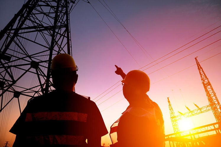 Two electricians looking at electrical tower