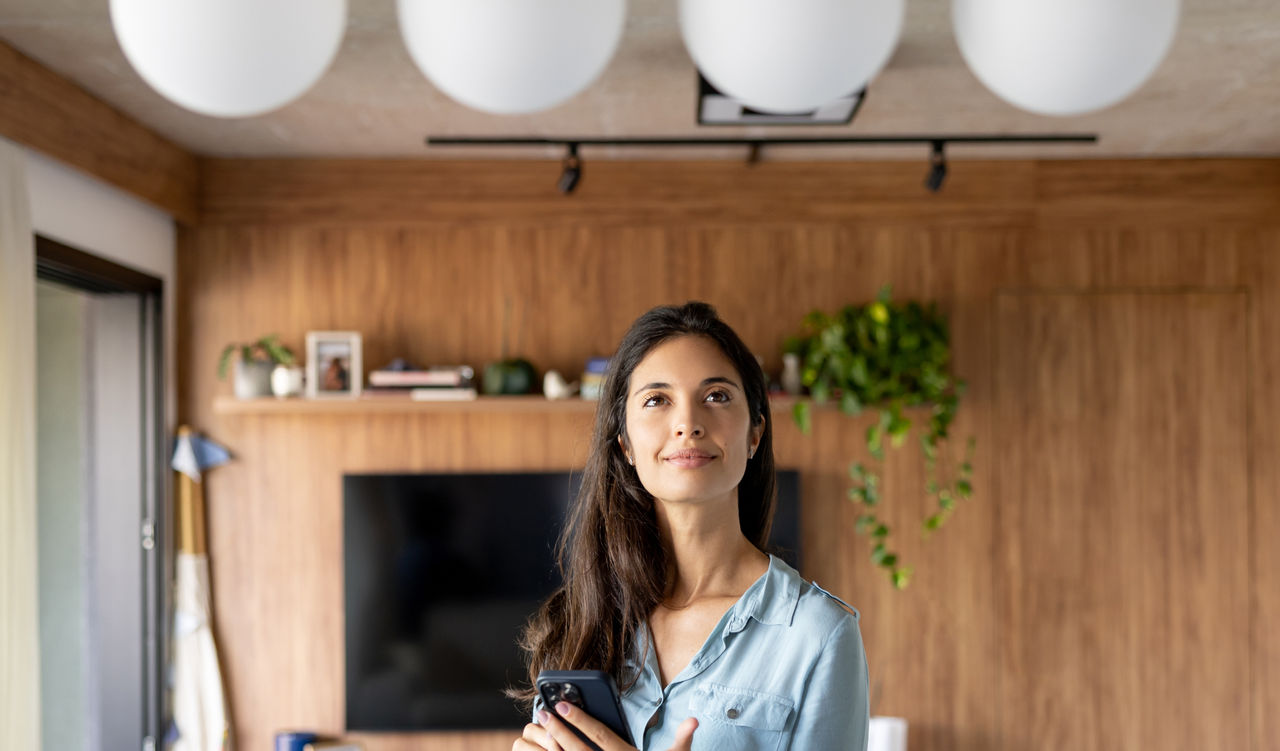 Brazilian woman controlling a lamp in her house using an automated system - technology concepts